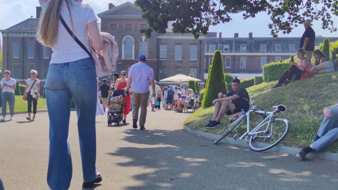 People walking and sitting on the grass in Kensington Gardens on a sunny day, a bicycle on the lawn