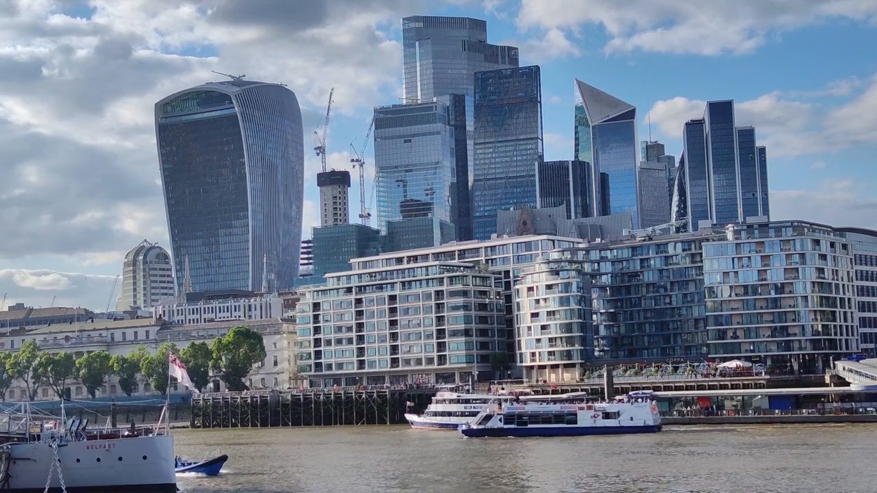 Glass skyscrapers of the City above the north bank of the Thames, with boats moored along the river