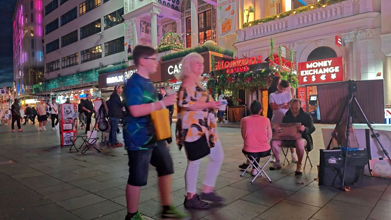 Street performers and a crowd on a paved square at night, with lit-up shopfronts behind