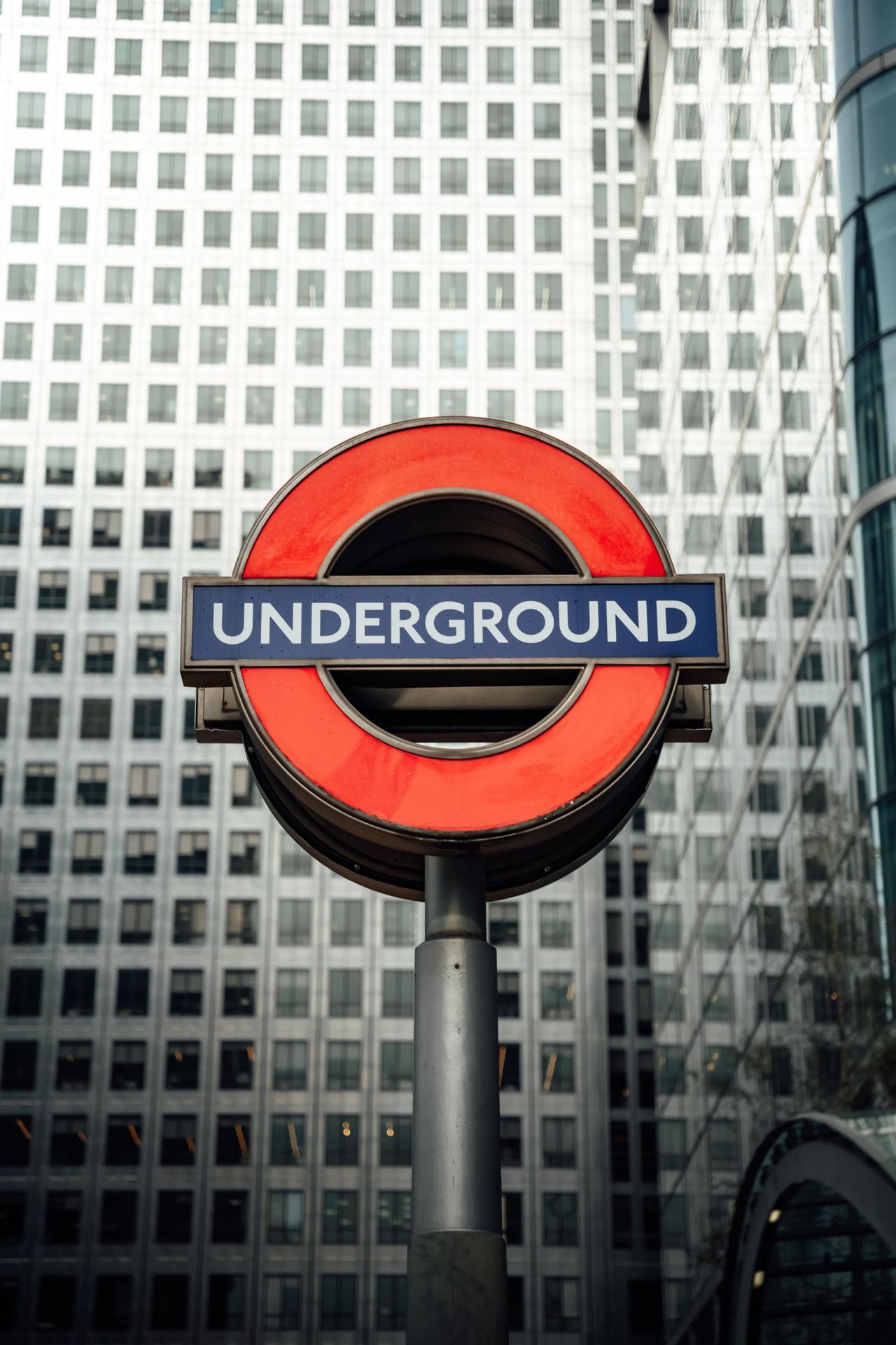 Underground roundel on a post in front of a tall glass office tower