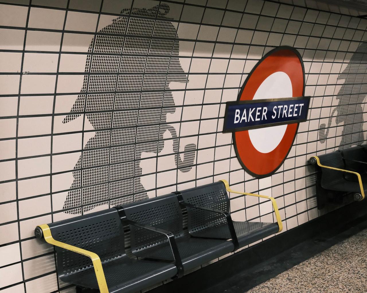 Baker Street roundel on a tiled platform wall beside a Sherlock Holmes silhouette, with benches below