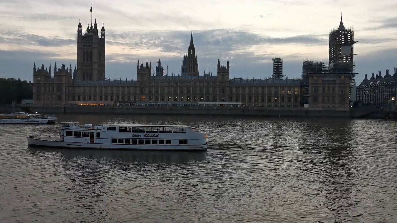 The Houses of Parliament seen across the Thames on a grey day, with a tour boat on the river