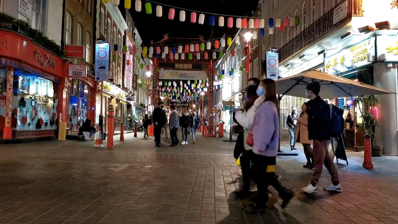 A pedestrian street in Chinatown at dusk, with strings of lanterns overhead and people walking